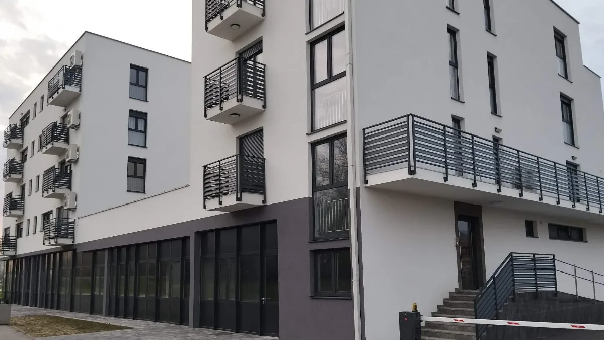 Nova stambena zgrada sa ravnim krovom u Požegi. Moderno dizajnirana sa bijelom fasadom i antracit crnim prozorima, vratima te balkonskim ogradama.
